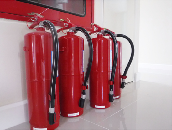 Four red fire extinguishers lined up against a wall on a grey tile floor